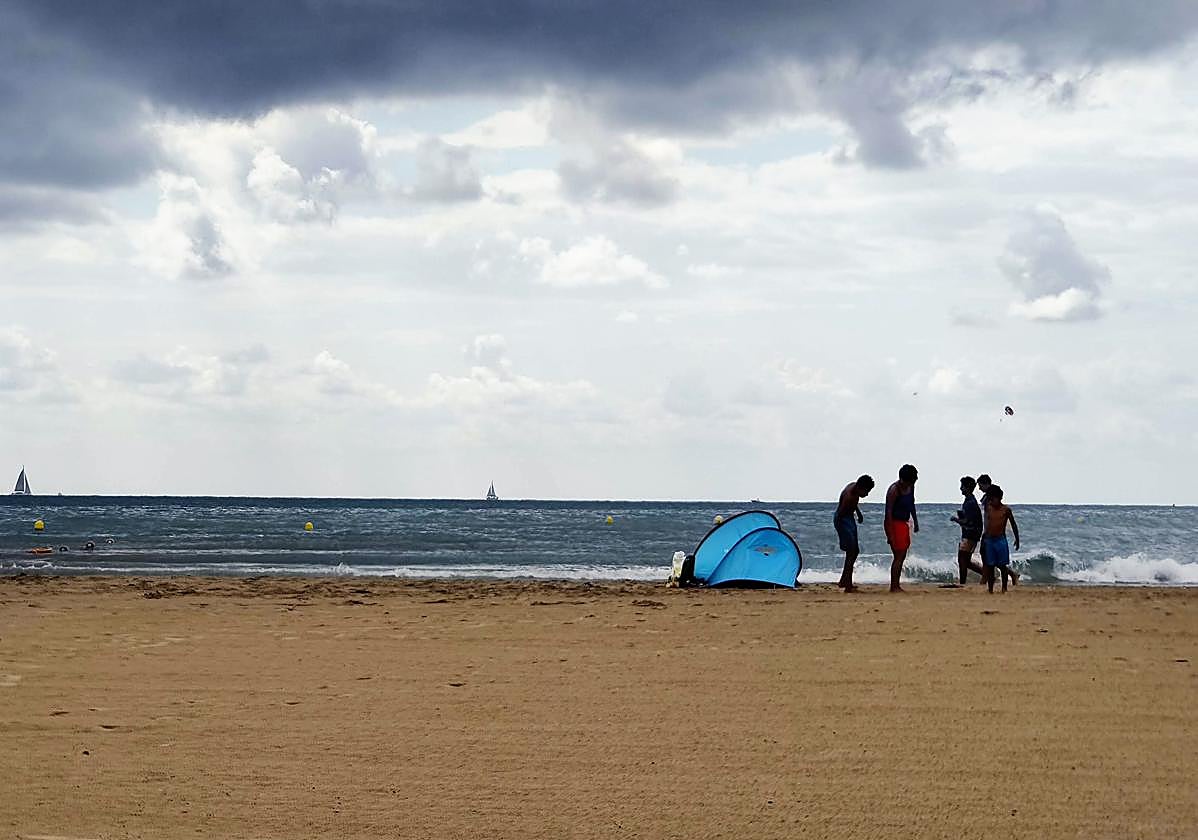 Un grupo de niños disfruta de la playa en un día nublado.