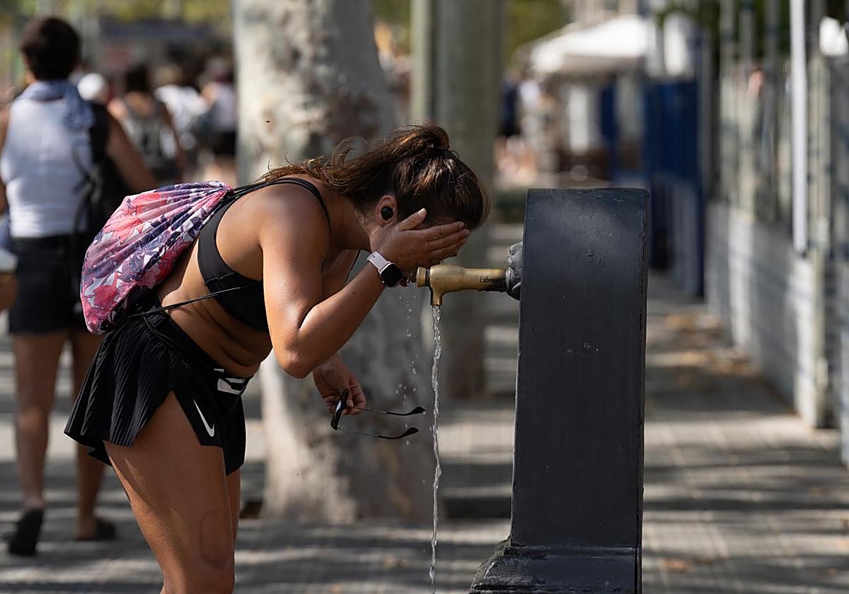 Una viandante se moja la cabeza para combatir el calor en plena calle.