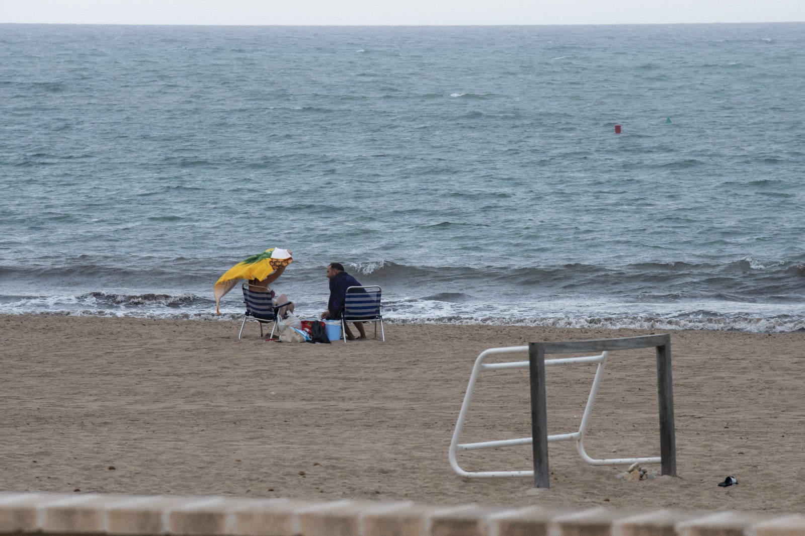 Varias personas desafían a la lluvia en una playa de Alicante.