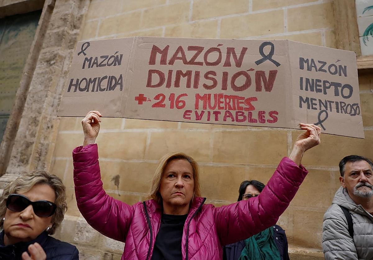Una mujer porta una pancarta contra el presidente Mazón, a la puertas de Les Corts.