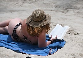 Una mujer lee un libro en la playa del Postiguet de Alicante.