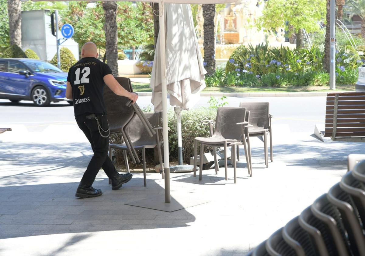 Un camarero saca sillas a una terraza de Alicante.