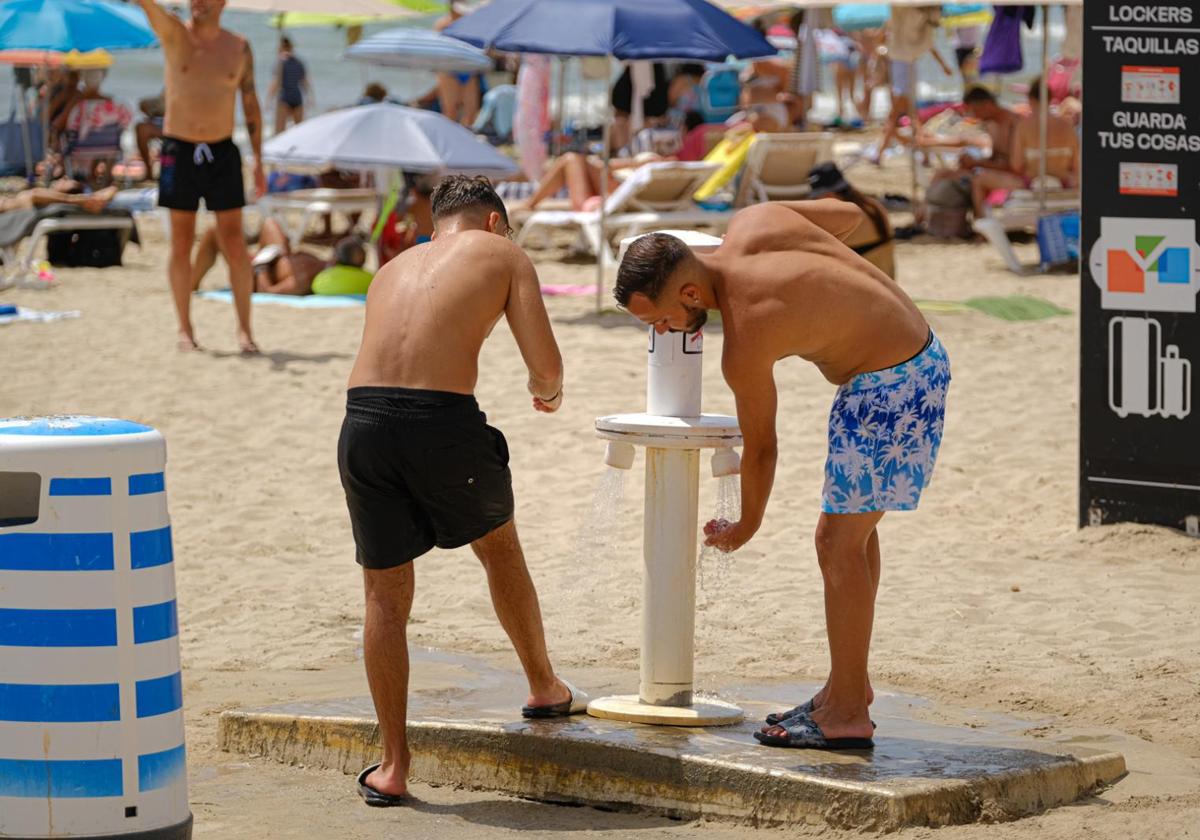 Two bathers refresh themselves in the showers at Postiguet beach.
