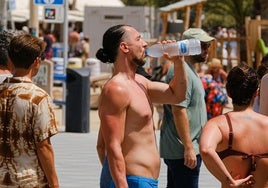 Una persona se refresca con agua fría en la playa del Postiguet de Alicante.