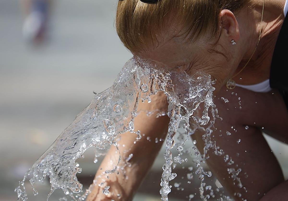 Una mujer se refresca en una fuente pública.