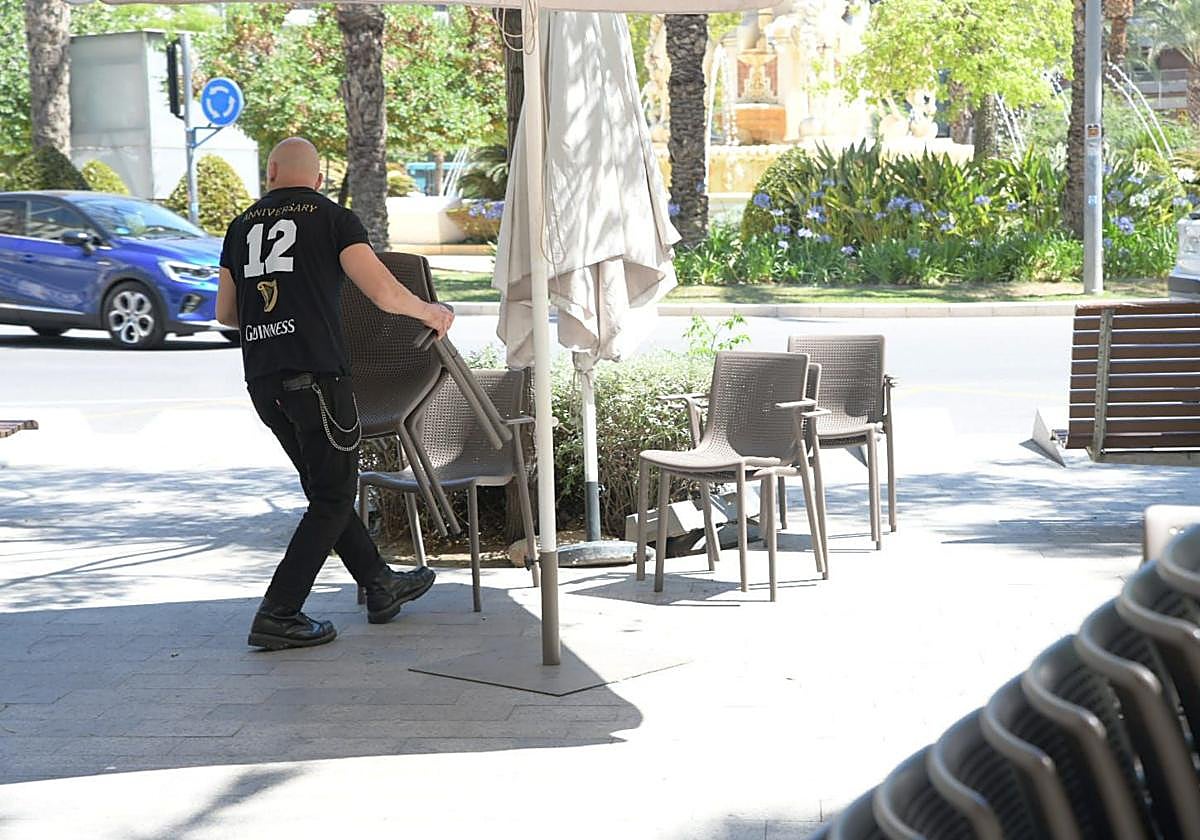 Un camarero recoge sillas en una terraza.