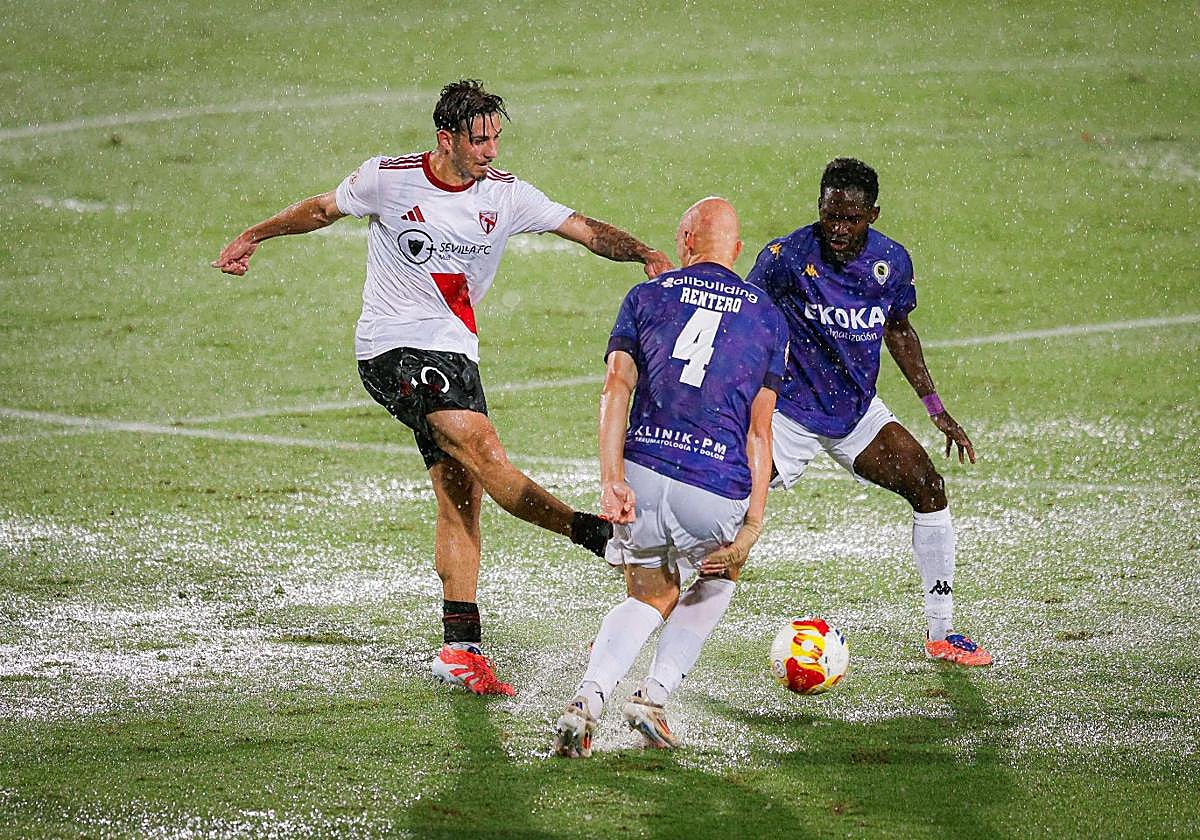Rentero y Ben Hamed tratan de interceptar un pase de un jugador sevillista con el terreno completamente encharcado por la lluvia.