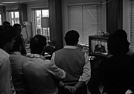 Un grupo de personas se juntan delante de la televisión para oír el anuncio de la muerte de Francisco Franco.