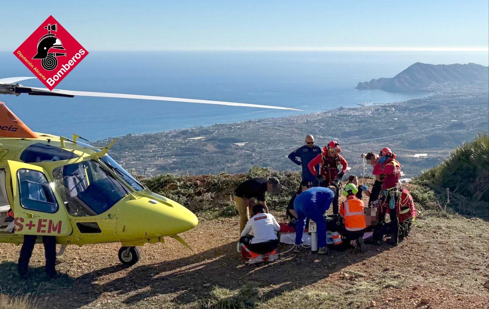 Various personnel attend to the collapsed hiker while on a mountain route.
